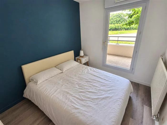 Chambre meublée, mur bleu et fenêtre sur la verdure